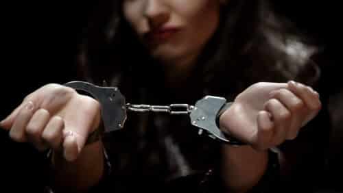 Woman holding her hands forward in handcuffs under dim light during a stylised roleplay shoot