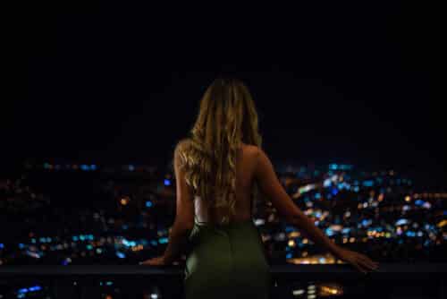 Elegant woman in a backless green dress overlooking the London city skyline at night
