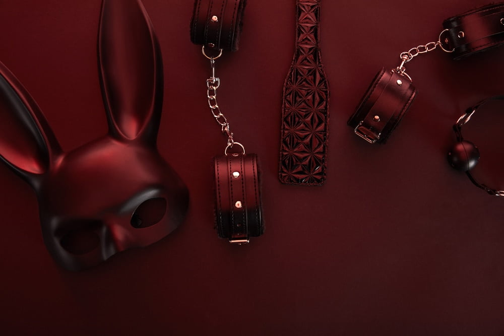Artistic flat lay of black leather accessories and a mask on red background