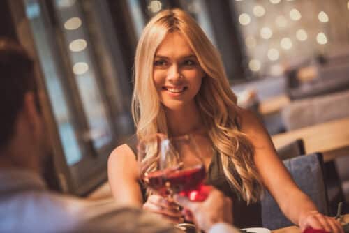 Smiling woman with long blonde hair enjoying wine at a London restaurant during an evening out