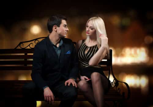 Blonde Escort’s Power Play near Oxford Circus sitting on a bench in London at night, sharing a confident look